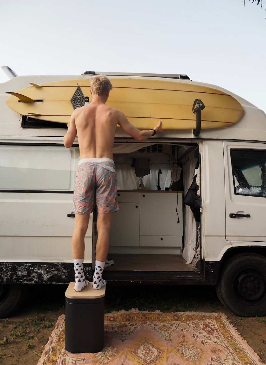 Mann steht auf Trelino® Origin L Trenntoilette und befestigt Surfbrett an Camper.