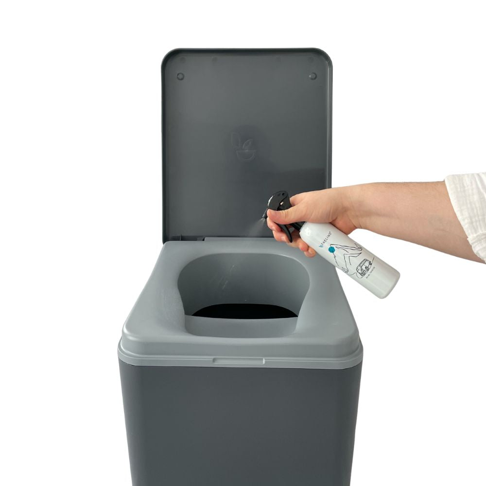 Hellgraue Sprayflasche mit weißem Etikett und schwarzem Sprühkopf neben offenem grauem Trenntoilettensitz.