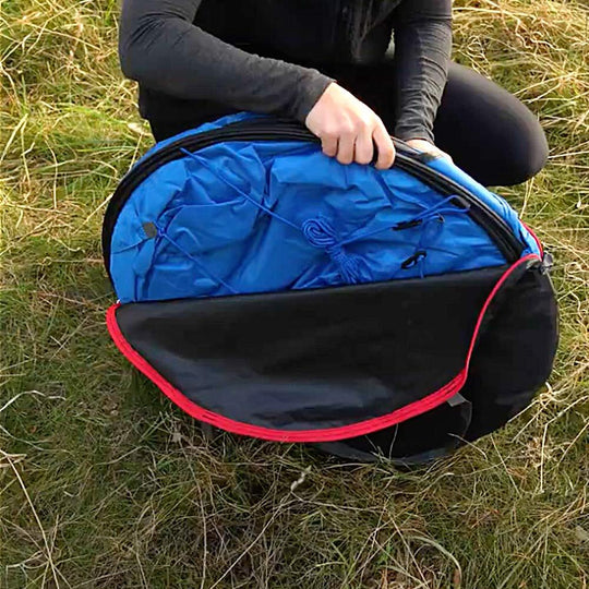 Blauer und schwarzer Pop-up-Toilettenzelt faltbar mit rotem Rand im Gras geöffnet.