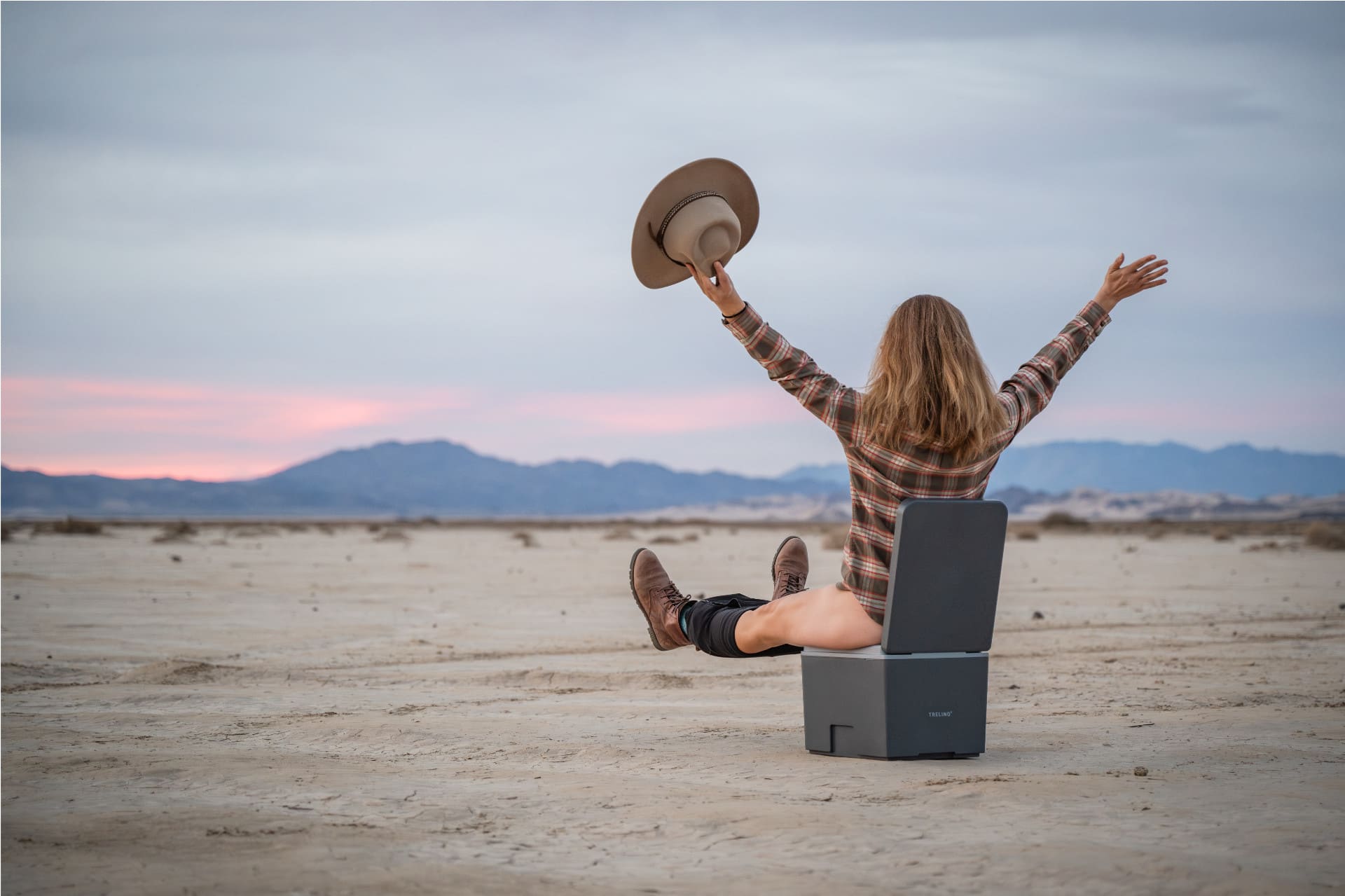 Frau in Wüeste auf Trelino Evo S Trenntoilette/ Campingtoilette, die ihre Arme und Beine vor Freude hebt.